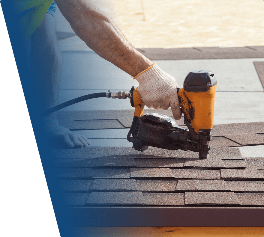 A person wearing a white glove is using a yellow pneumatic nail gun to install brown asphalt shingles on a roof. The shingles are being aligned in overlapping rows. The background shows a blurred outdoor area.