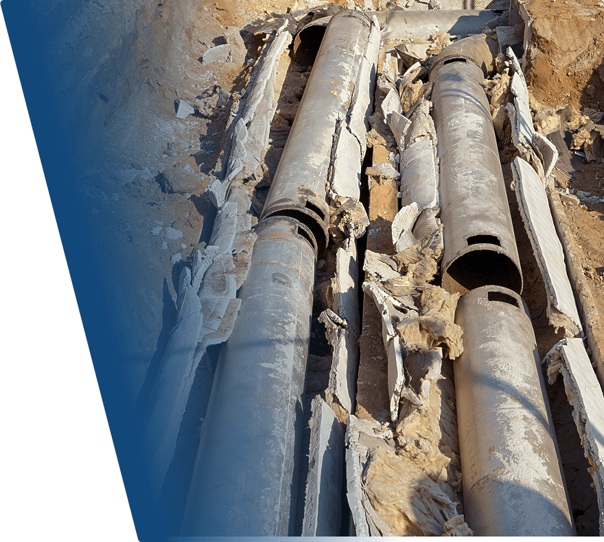 Two large metal pipes partially buried in the ground with damaged and torn insulation material surrounding them. The pipes appear weathered and are set in a trench filled with dirt.
