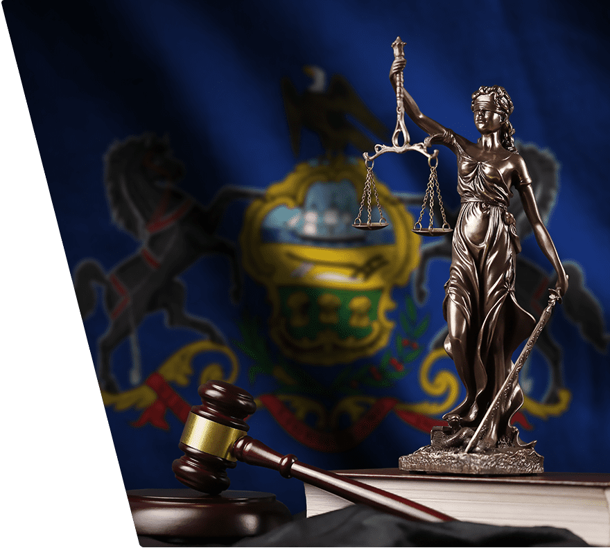 A bronze statue of Lady Justice holding scales and a sword stands on a book, next to a wooden gavel with a gold band. The background features a blurred Pennsylvania state flag.